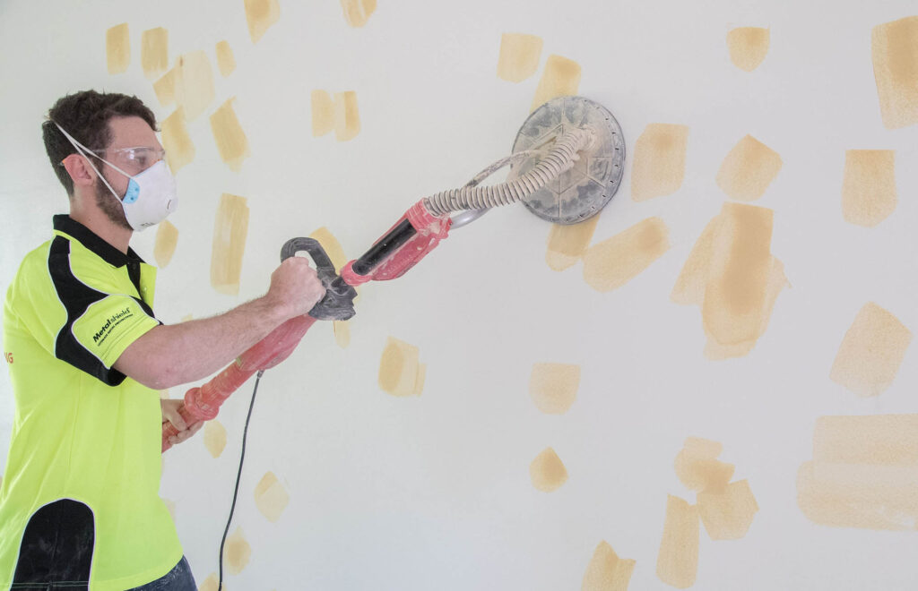 A person using an electric sander to remove wallpaper.