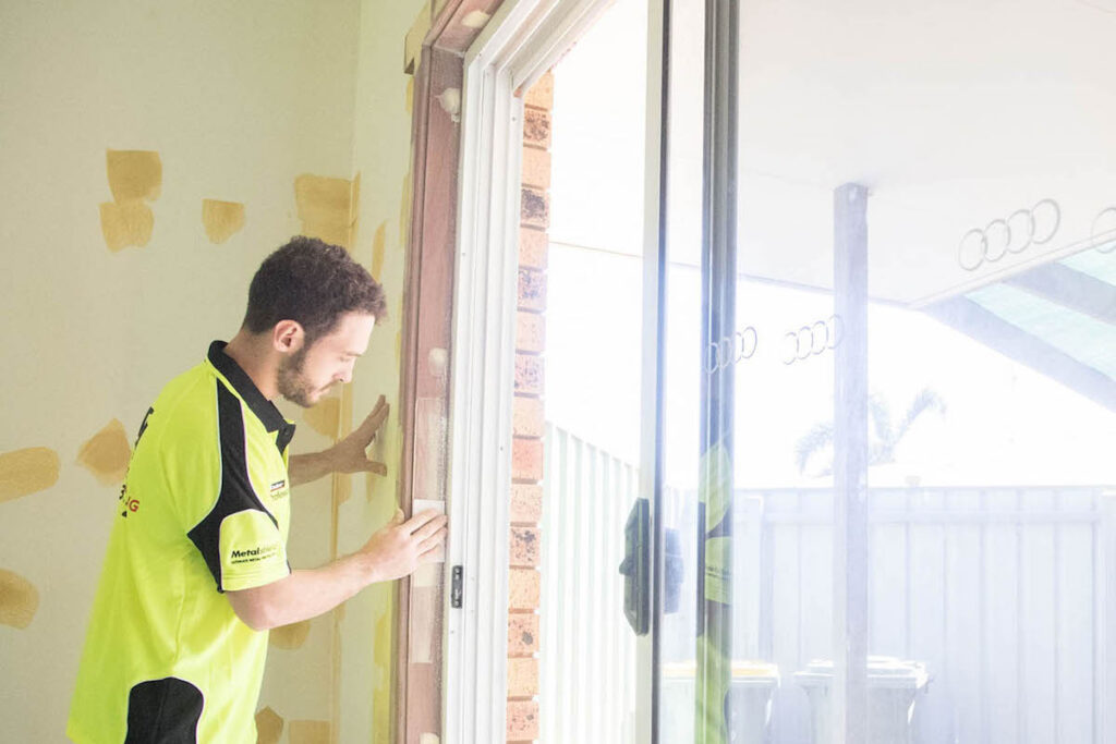 A man in yellow shirt standing next to sliding glass door.