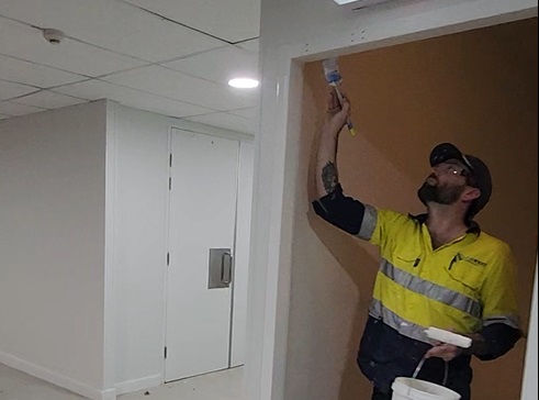 A man in yellow shirt painting wall.