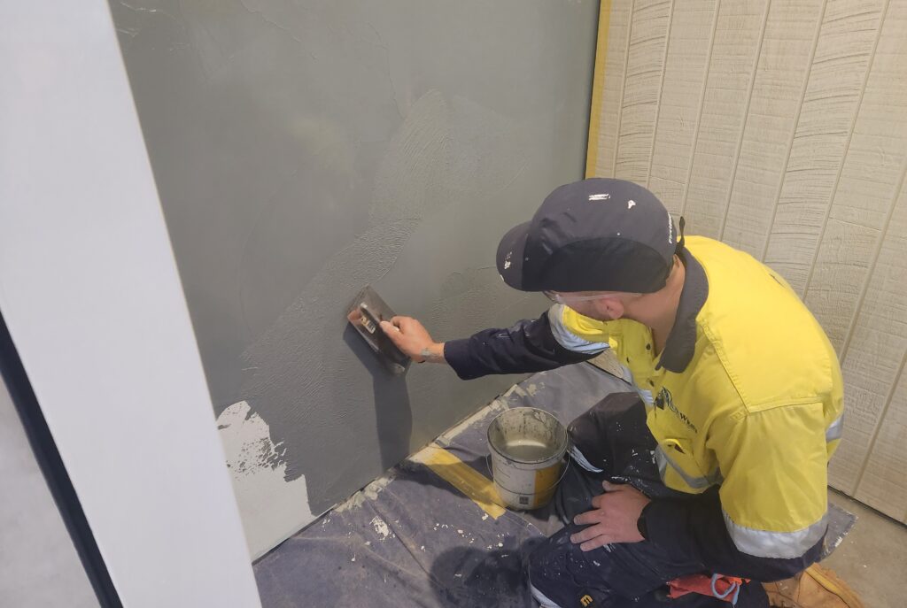 A man in yellow shirt painting wall with black paint.