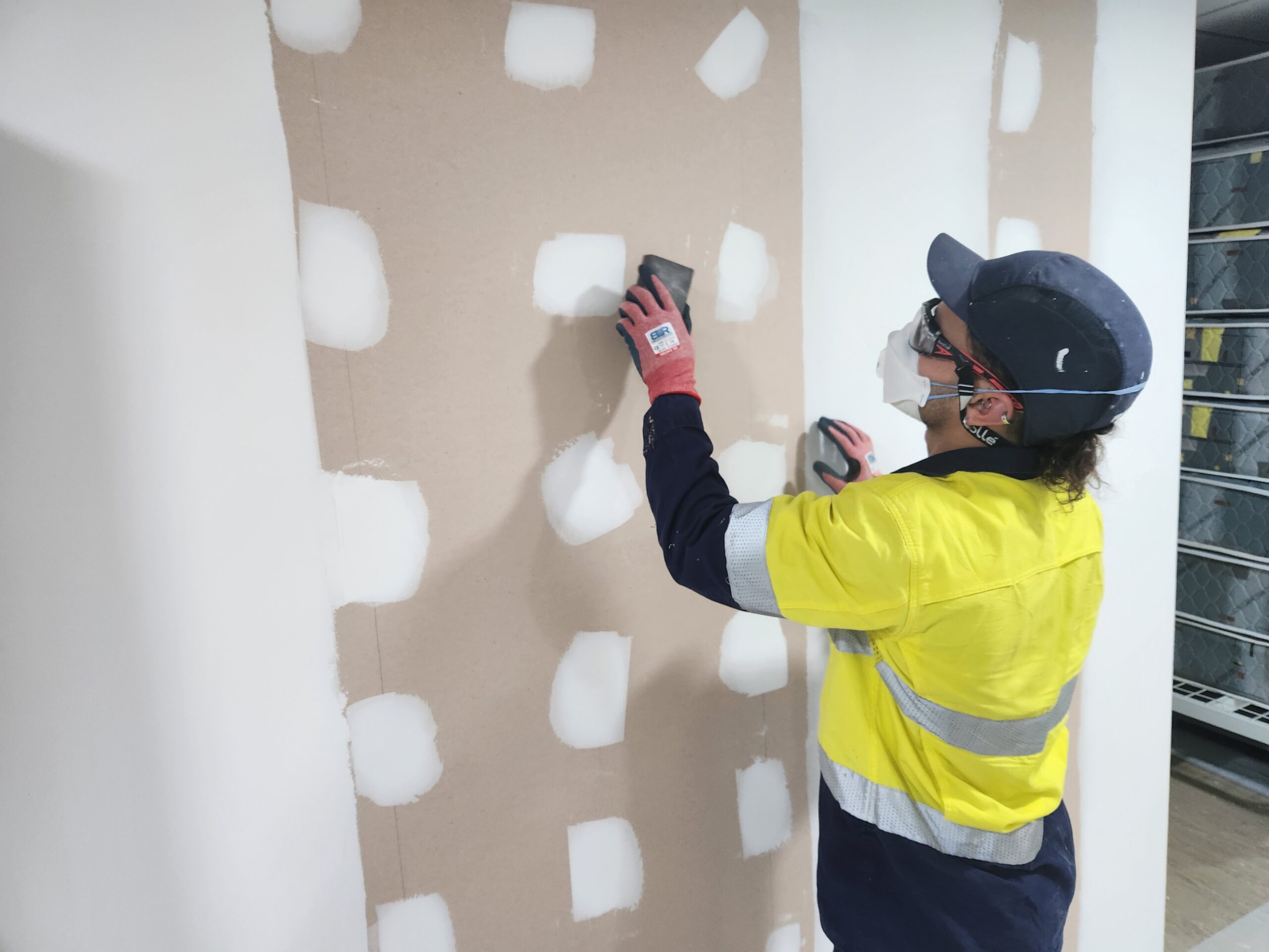 A man in yellow vest and hard hat painting wall.