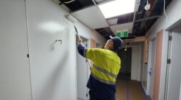 A man in yellow vest painting the ceiling of a room.