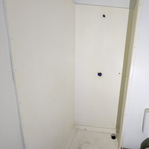 A white shower stall with no door and black knobs.